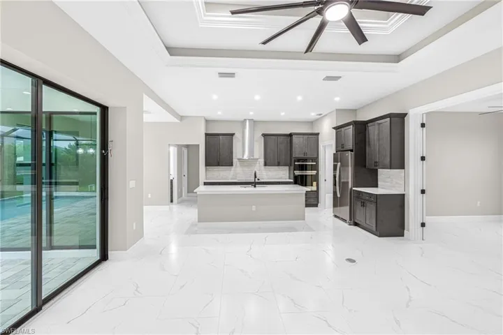 Kitchen with ceiling fan, a tray ceiling, light marble finish floors, a kitchen island with sink, and ornamental molding