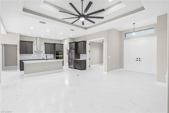 Unfurnished living room featuring a raised ceiling, light marble finish flooring, a ceiling fan, and recessed lighting