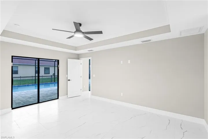 Spare room with a tray ceiling, ornamental molding, light marble finish flooring, and a ceiling fan