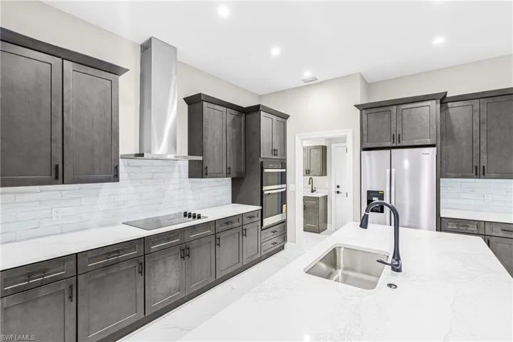 Kitchen featuring decorative backsplash, wall chimney range hood, appliances with stainless steel finishes, light stone countertops, and recessed lighting