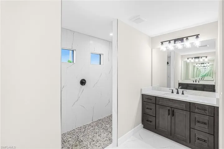 Bathroom with vanity, a marble finish shower, light marble finish flooring, and recessed lighting