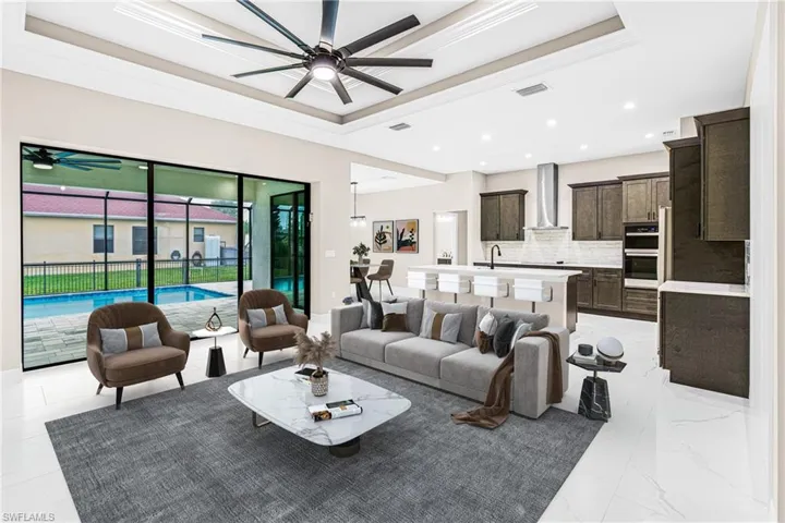 Living area with a tray ceiling, a ceiling fan, ornamental molding, light marble finish flooring, and recessed lighting