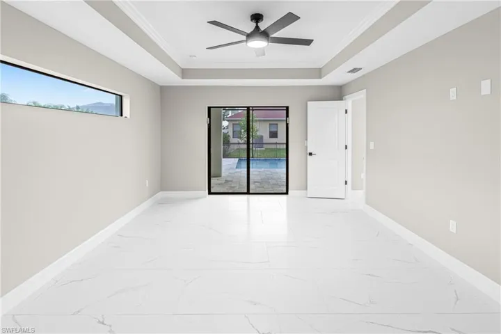 Spare room featuring light marble finish flooring, ornamental molding, a tray ceiling, and ceiling fan