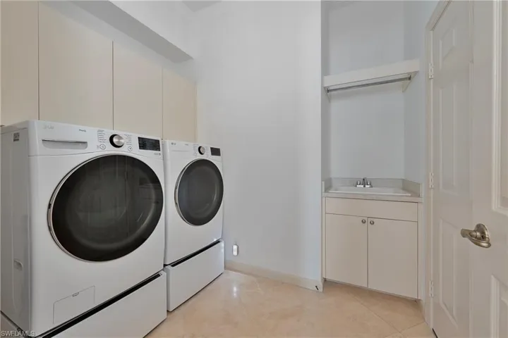Laundry area featuring washing machine and clothes dryer, cabinet space, light tile patterned flooring, and baseboards