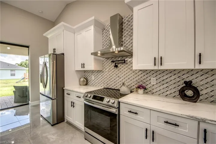 Kitchen featuring tasteful backsplash, stainless steel appliances, light stone countertops, white cabinetry, and wall chimney exhaust hood