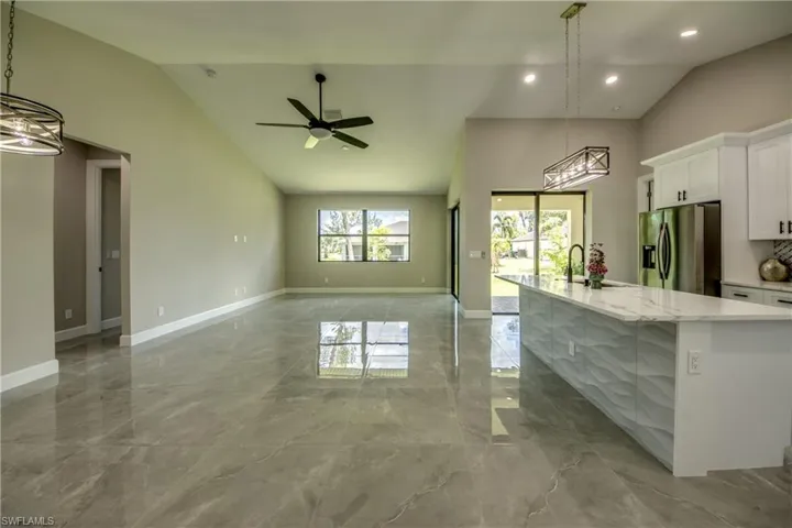 Kitchen featuring stainless steel fridge, an island with sink, light tile patterned floors, and hanging light fixtures