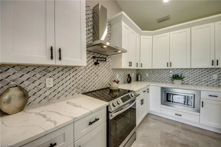 Kitchen featuring tasteful backsplash, stainless steel appliances, white cabinets, wall chimney exhaust hood, and light stone counters