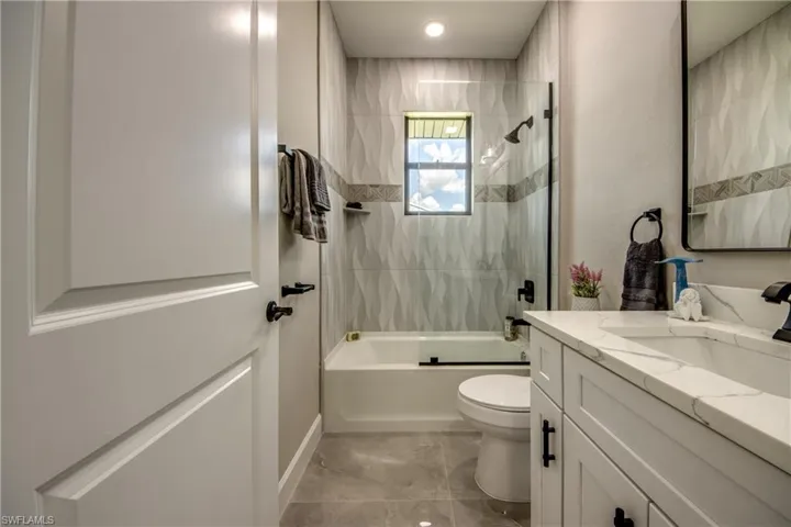 Full bathroom with vanity, tiled shower / bath, tile patterned floors, and toilet