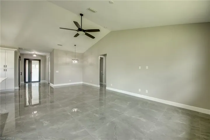 Empty room with light tile patterned floors, ceiling fan, and high vaulted ceiling