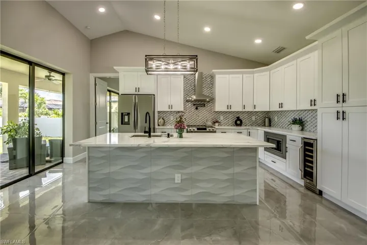 Kitchen with white cabinets, stainless steel appliances, an island with sink, light tile patterned flooring, and wall chimney exhaust hood