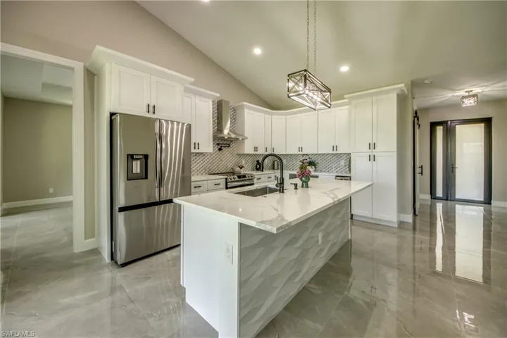 Kitchen with hanging light fixtures, white cabinetry, wall chimney exhaust hood, and stainless steel appliances