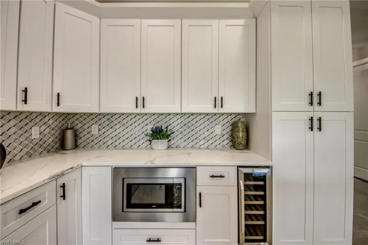 Kitchen featuring white cabinets, light stone counters, stainless steel microwave, backsplash, and wine cooler