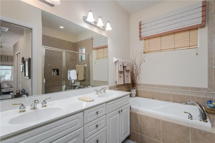 Full bathroom featuring ensuite bathroom, double vanity, a garden tub, and a stall shower
