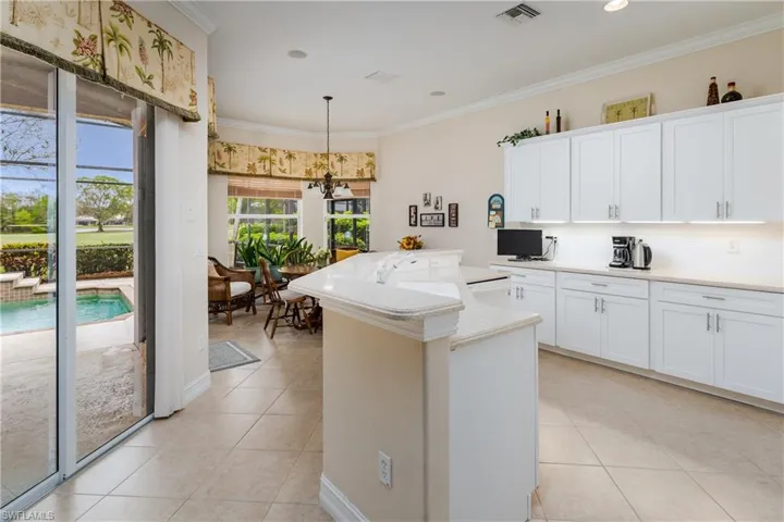 Kitchen with ornamental molding, a center island with sink, white cabinetry, light tile patterned floors, and backsplash