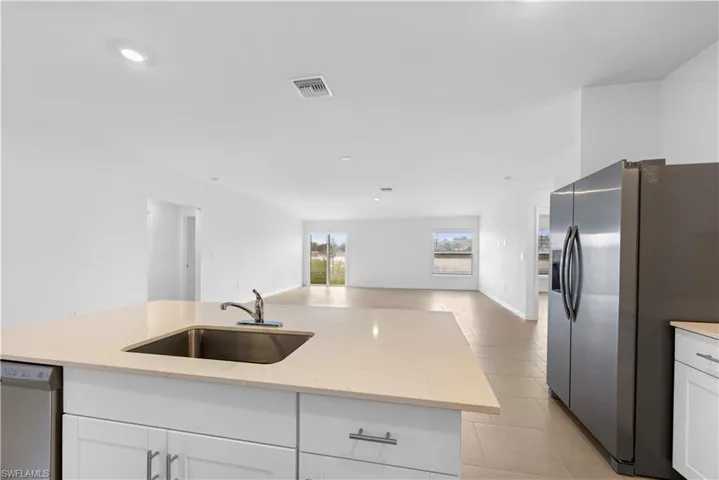 Kitchen with stainless steel appliances, light stone counters, open floor plan, white cabinets, and a center island with sink