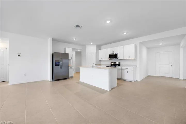 Kitchen featuring stainless steel appliances, light countertops, white cabinetry, and a kitchen island with sink