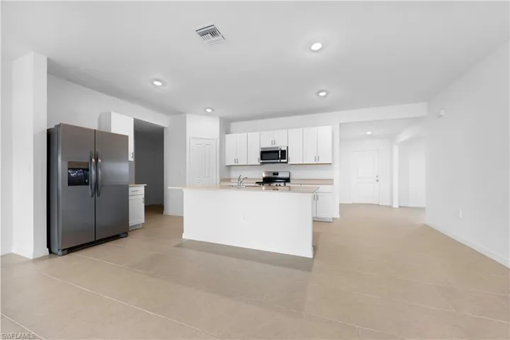Kitchen featuring stainless steel appliances, white cabinetry, a center island with sink, light stone counters, and recessed lighting