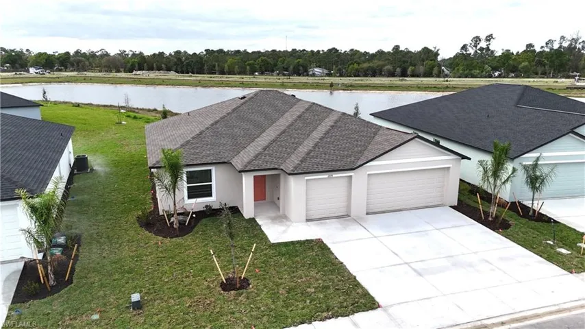 Ranch-style home with roof with shingles, a garage, a front lawn, stucco siding, and a water view