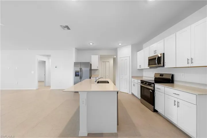 Kitchen featuring stainless steel appliances, a kitchen island with sink, white cabinets, recessed lighting, and light stone countertops