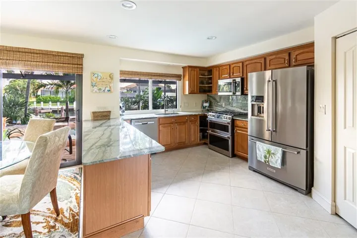 Kitchen featuring appliances with stainless steel finishes, a peninsula, glass insert cabinets, light stone countertops, and brown cabinets
