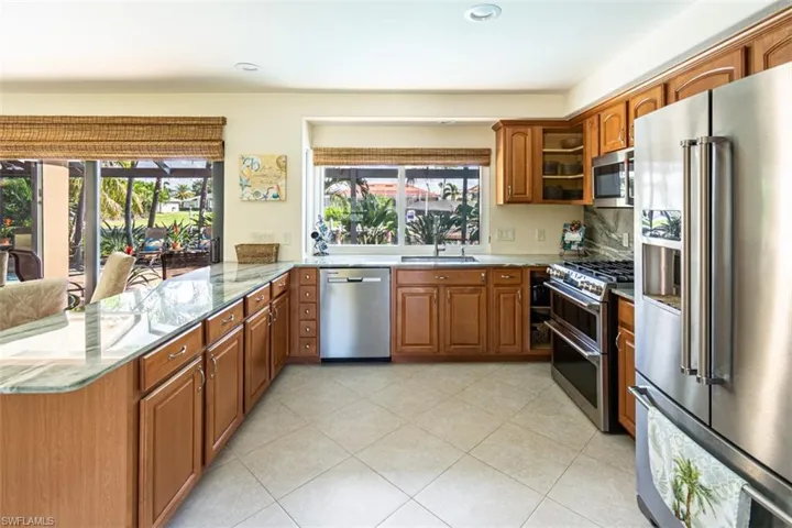 Kitchen with appliances with stainless steel finishes, brown cabinetry, a peninsula, light stone countertops, and recessed lighting