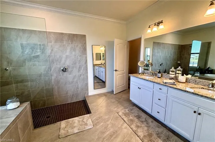 Bathroom with double vanity, walk in shower, crown molding, and light tile patterned flooring