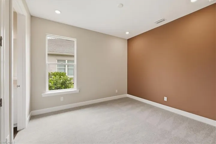 Spacious room featuring plush carpet flooring, recessed ceiling lighting, a prominent accent wall, and a single-pane window with white trim