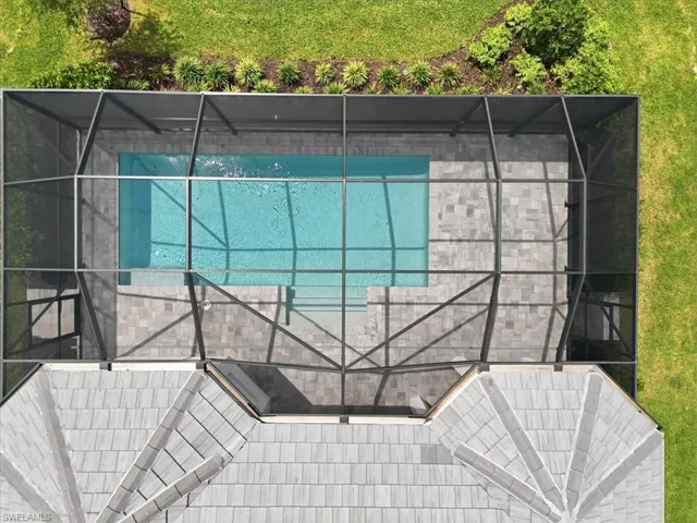 Screened-in rectangular swimming pool featuring a light blue finish and integrated steps, surrounded by a paver deck