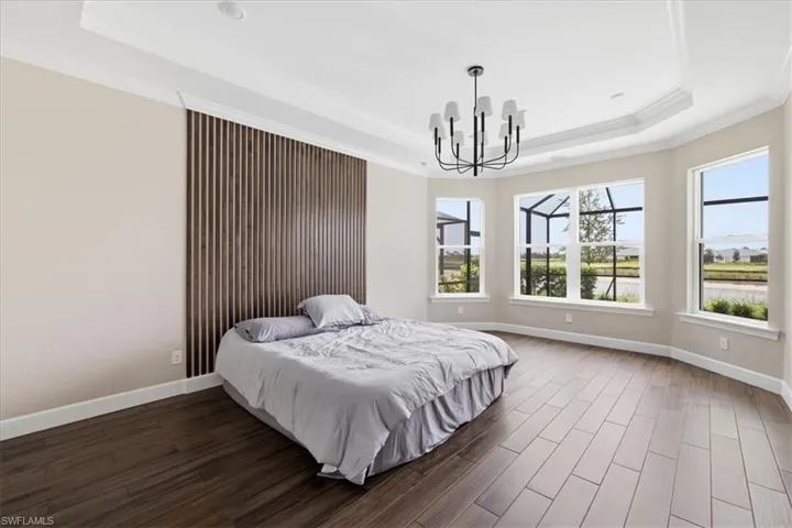 Wood-finish flooring throughout, featuring a tray ceiling with crown molding and a contemporary black chandelier