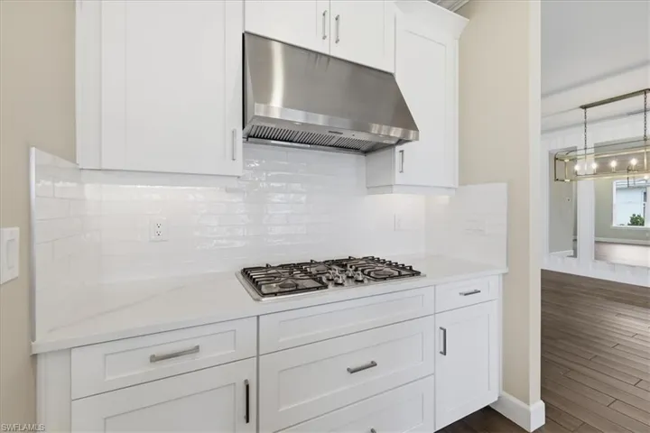Modern kitchen featuring white shaker cabinetry, stainless steel range hood, built-in gas cooktop, white subway tile backsplash, and light-toned countertops