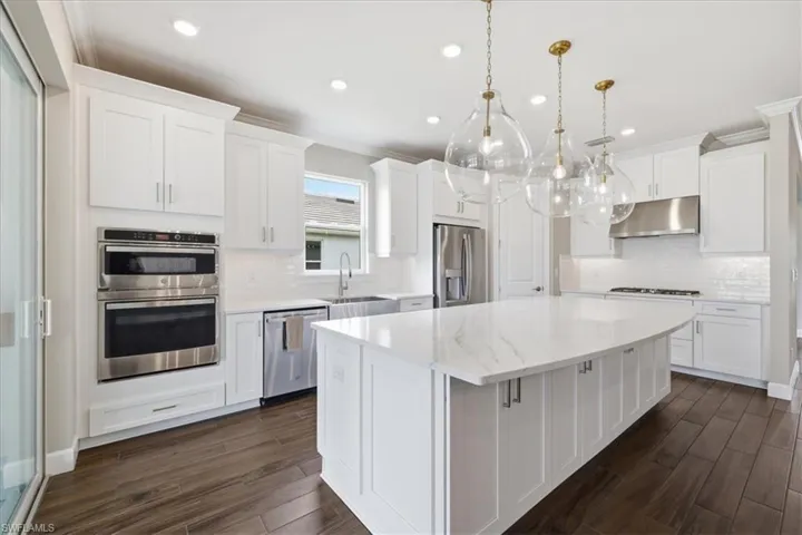 Expansive kitchen featuring a large central island with a quartz countertop, white shaker-style cabinetry, stainless steel appliances, and wood-finish flooring