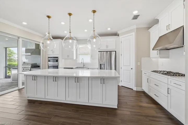 Kitchen featuring a large central island with pendant lighting, white shaker cabinetry, stainless steel appliances, and wood-finish flooring