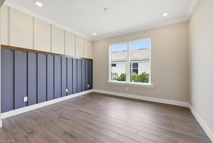 Room featuring wood-finish flooring, a decorative accent wall with vertical paneling, and crown molding