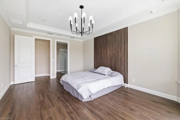 Spacious room featuring wood-finish flooring, a tray ceiling with crown molding, a modern chandelier, and a decorative slatted wood accent wall