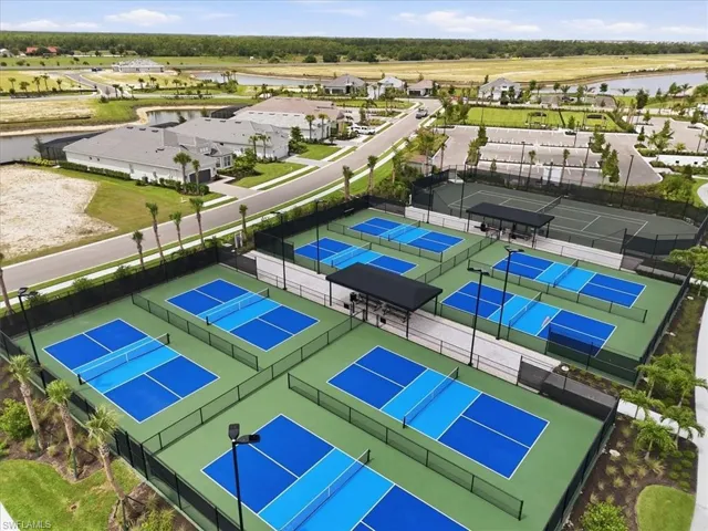 Multiple pickleball courts with blue and light blue playing surfaces, dark green surrounding areas, and black perimeter fencing