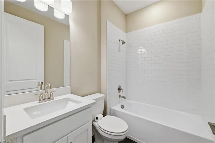 Contemporary bathroom featuring a white subway tile tub surround, white vanity with an integrated sink, brushed nickel fixtures, and overhead vanity lighting