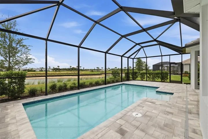 Screened-in outdoor living space featuring a rectangular pool with a shallow entry area, a spacious paver patio, and a distant water feature