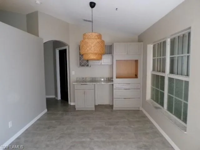 Kitchen with vaulted ceiling, light countertops, arched walkways, pendant lighting, and light floors