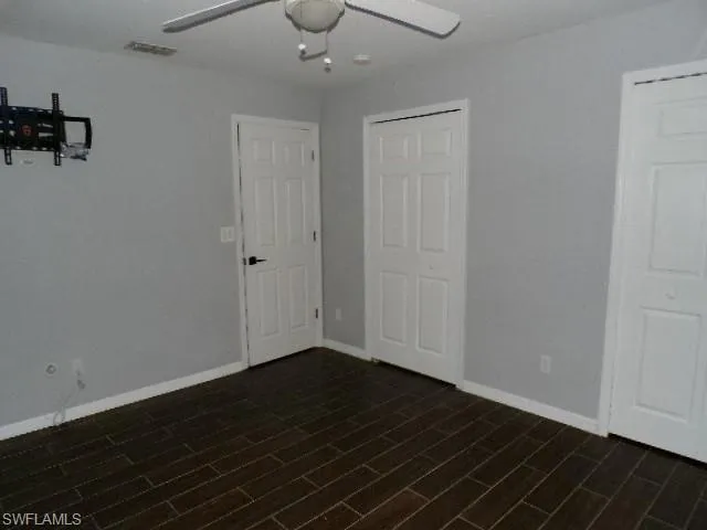 Unfurnished bedroom featuring a ceiling fan, multiple closets, and dark wood-type flooring