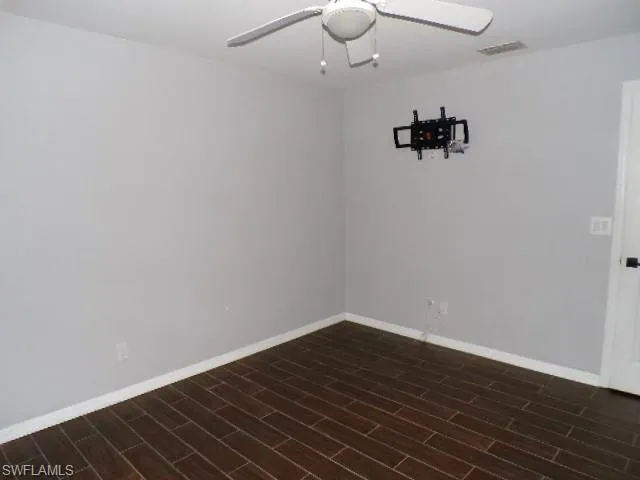 Empty room featuring a ceiling fan and dark wood-type flooring