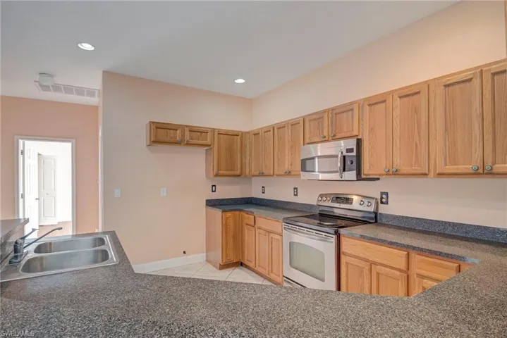 Kitchen featuring stainless steel appliances, light tile patterned floors, dark countertops, and recessed lighting