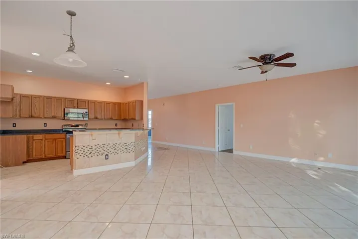 Kitchen with decorative light fixtures, a kitchen breakfast bar, stainless steel appliances, open floor plan, and light tile patterned flooring