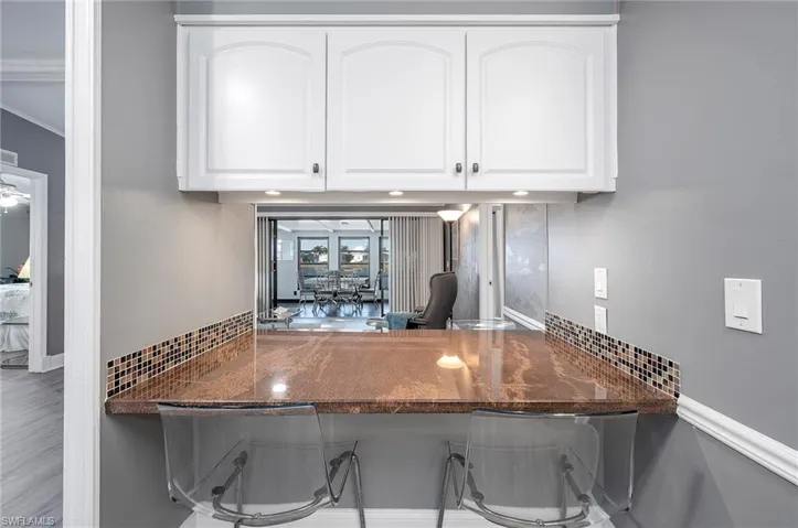 Bar with tasteful backsplash, white cabinetry, and dark stone countertops