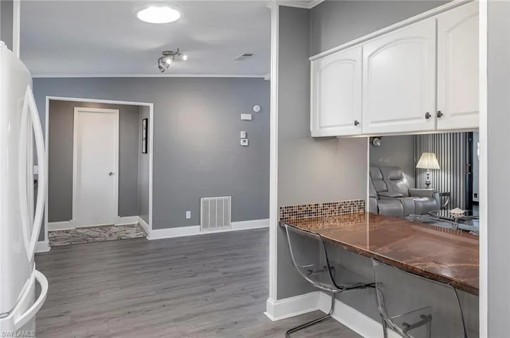 Kitchen with white cabinetry, white refrigerator, wood-type flooring, vaulted ceiling, and ornamental molding