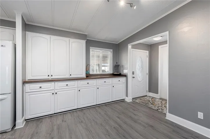 Kitchen with light wood-type flooring, ornamental molding, white refrigerator, white cabinetry, and lofted ceiling