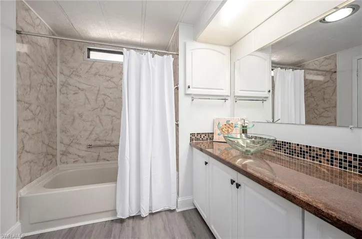 Bathroom with hardwood / wood-style flooring, shower / bath combination with curtain, decorative backsplash, and vanity