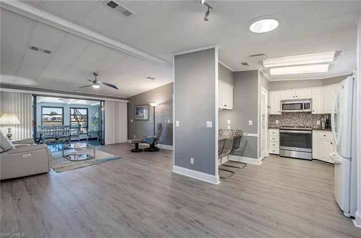Living room featuring lofted ceiling with beams, light hardwood / wood-style floors, ceiling fan, and crown molding