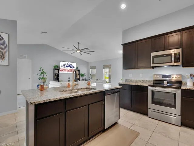 Kitchen featuring appliances with stainless steel finishes, lofted ceiling, dark brown cabinetry, and sink