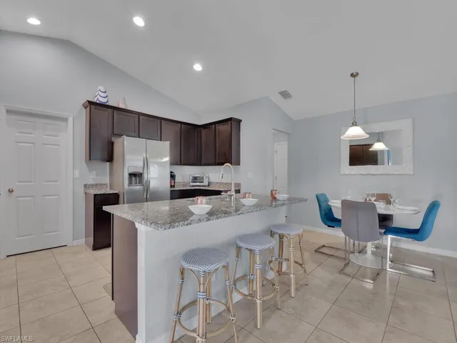 Kitchen with light tile patterned floors, stainless steel fridge with ice dispenser, vaulted ceiling, dark brown cabinetry, and light stone counters