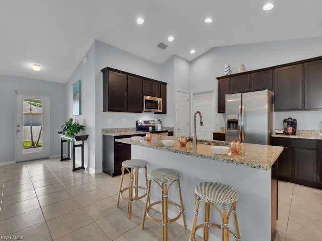 Kitchen with light stone countertops, stainless steel appliances, lofted ceiling, light tile patterned floors, and a center island with sink